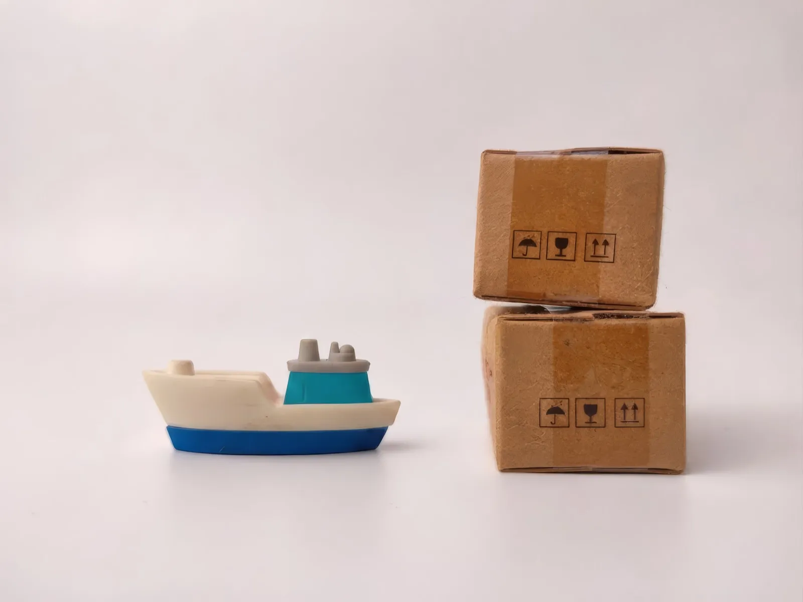 Toy cargo ship beside small parcel boxes — from single shipments to full loads