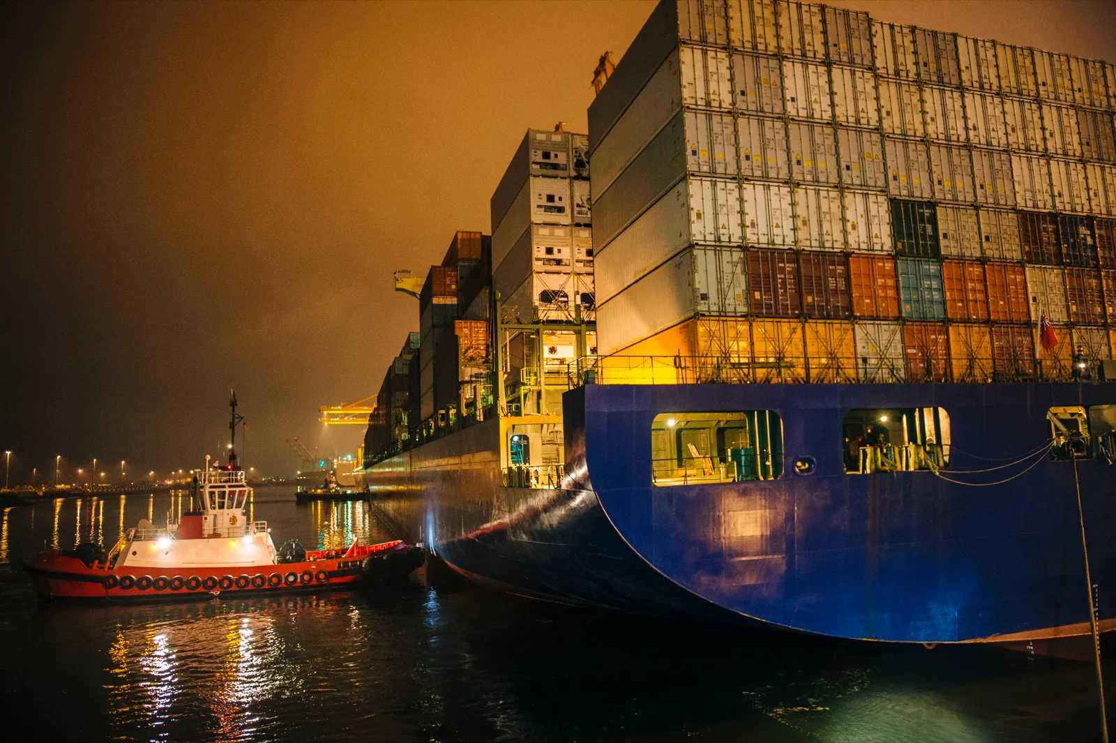 Tugboat manoeuvring a container ship on the river at night
